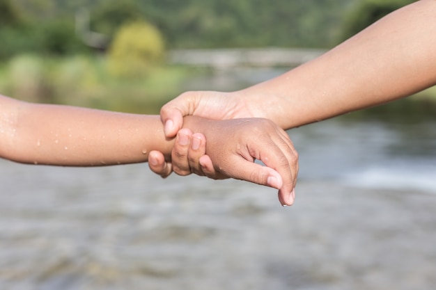 Chiuda sulla donna che tiene la sua mano della figlia nel fiume. Concetto di aiuto