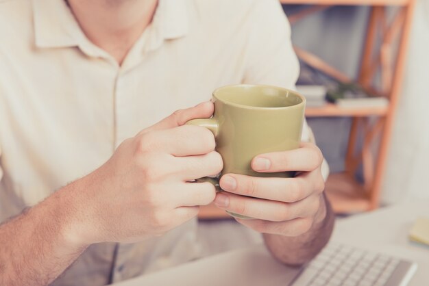 Chiuda sulla foto delle mani dell'uomo che tengono la tazza con il tè