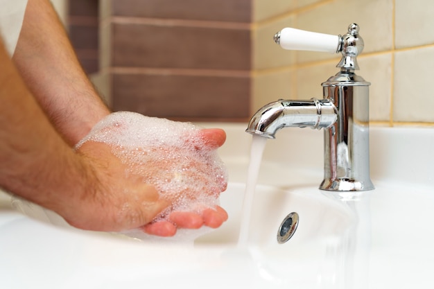 Chiuda sulla foto delle mani maschii che lavano con il sapone sopra il lavandino