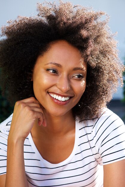 Chiuda sulla giovane donna africana con capelli ricci che distoglie lo sguardo e che sorride all&#39;aperto