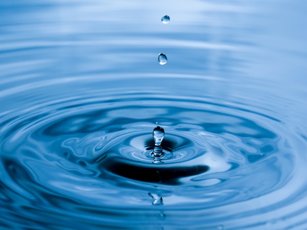 Chiuda sulla goccia di acqua su fondo blu