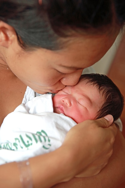 Chiuda sulla madre che bacia il bambino infantile in lei armi