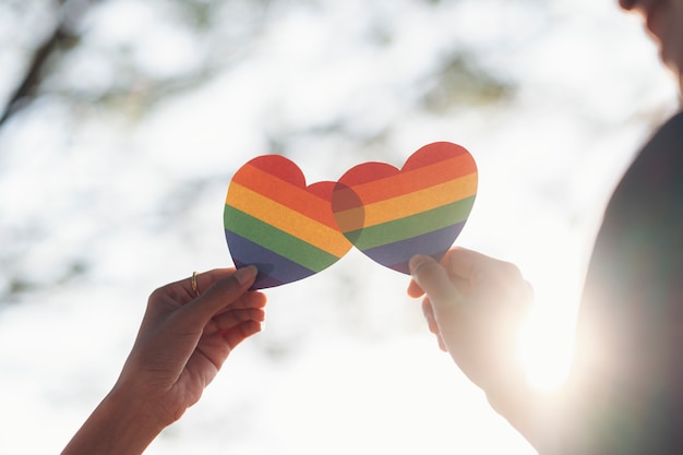 Chiuda sulla mano del cuore dell'arcobaleno della tenuta delle coppie di LGBTQ.