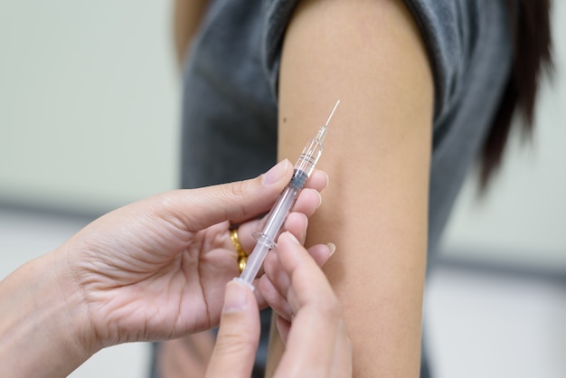 Chiuda sulla mano del medico che inietta per la vaccinazione nel paziente della donna della spalla.