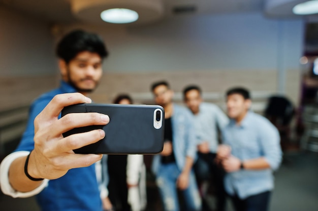 Chiuda sulla mano dell'uomo asiatico che tiene il telefono cellulare e che fa selfie con gli amici.