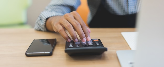 Chiuda sulla mano dell&#39;uomo del proprietario di affari facendo uso del calcolatore per lavorare all&#39;ufficio