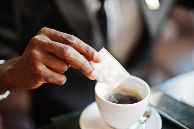 Chiuda sulla mano dell'uomo di affari che versa lo zucchero nel caffè