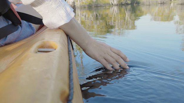 Chiuda sulla mano della donna adulta sulla barca della canoa del kayak su un lago che tocca l'acqua trasparente chiara