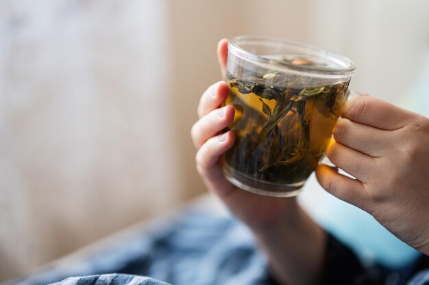 Chiuda sulla mano della donna che beve tè sul suo letto