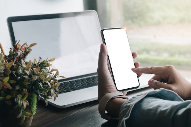 Chiuda sulla mano della donna facendo uso di uno Smart Phone con lo schermo in bianco alla caffetteria del caffè