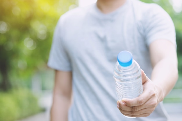 Chiuda sulla mano della giovane donna che tiene la bottiglia di acqua potabile fresca da una plastica nel parco.