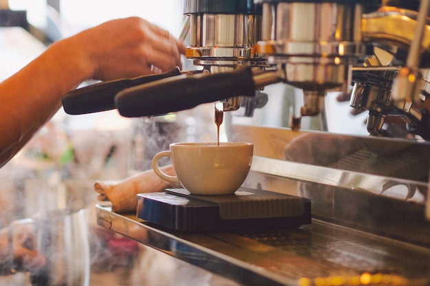 Chiuda sulla mano di barista che produce una tazza di caffè.