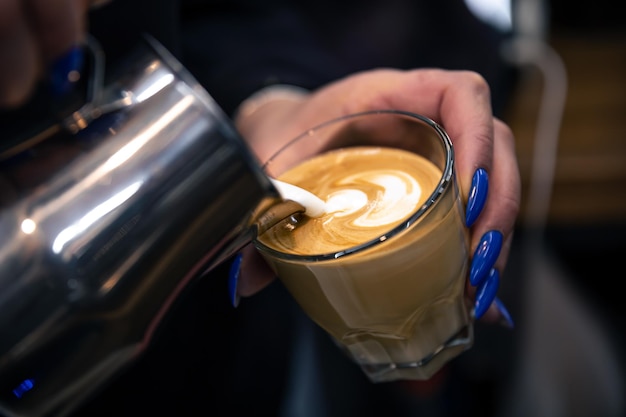 Chiuda sulla mano di una donna barista versando la schiuma di latte nel caffè espresso