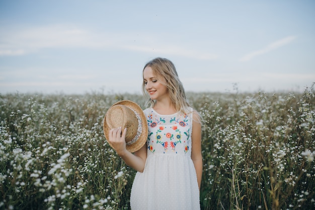Chiuda sulla ragazza del ritratto con un cappello in mano cammina in un campo con i fiori del campo e sorride sinceramente