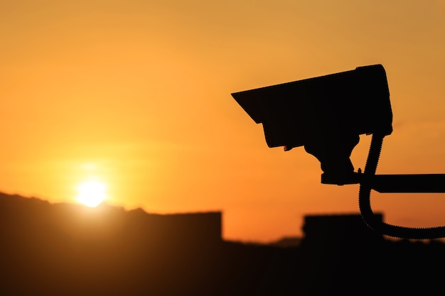 Chiuda sulla siluetta della macchina fotografica del CCTV di sicurezza con il fondo del tramonto