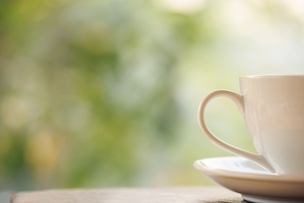 Chiuda sulla tazza di caffè macchiato sulla tavola in giardino con il bokeh della luce della sfuocatura