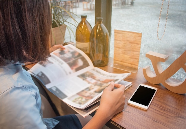 Chiuda sulla tenuta dell&#39;adolescente e la lettura della rivista al caffè