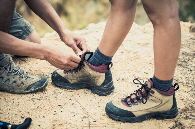 Chiuda sulla viandante maschio legami i lacci delle scarpe della viandante della femmina nella foresta