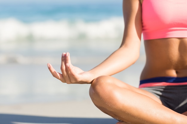 Chiuda sulla vista della donna adatta che fa l&#39;yoga al lato del mare