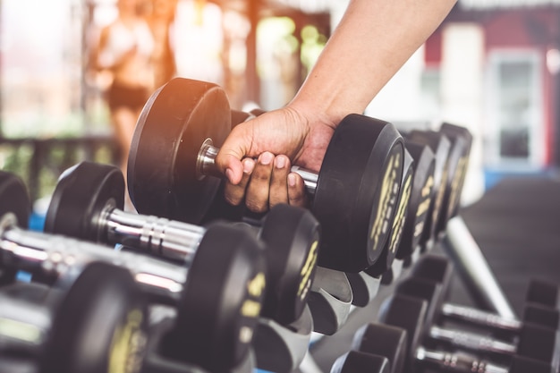 Chiuda sulla vista delle mani che selezionano dumbbell sullo scaffale in palestra