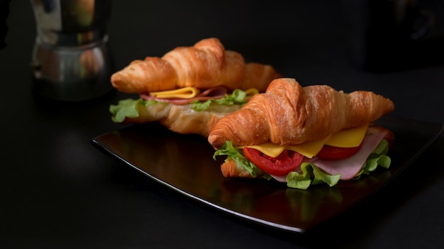 Chiuda sulla vista di un piatto del pasto della prima colazione con il prosciutto e il formaggio freschi del panino del croissant