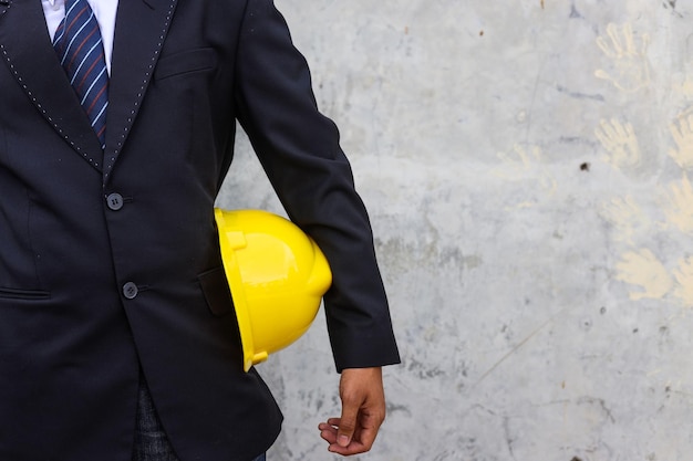 Chiuda sulla vista frontale dell'uomo d'affari di ingegneria in vestito che tiene il casco giallo di sicurezza per la sicurezza