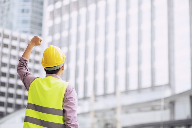 Chiuda sulla vista posteriore dell'operaio edile maschio di ingegneria che tiene il casco giallo di sicurezza e indossa indumenti riflettenti per la sicurezza dell'operazione di lavoro.