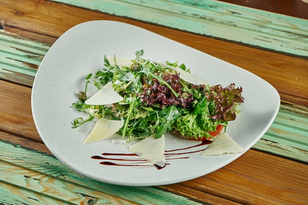 Chiuda sulla vista su insalata calda con parmigiano, rucola, lattuga condita con salsa al tartufo su un piatto bianco su un tavolo di legno. Alimenti sani per la dieta. Cibo vegetariano