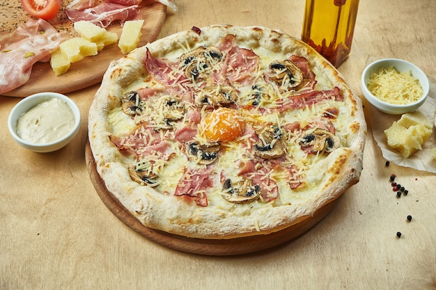 Chiuda sulla vista su pizza appetitosa con il prosciutto di Parma italiano, la salsa besciamella del tuorlo, funghi sulla tavola di legno in un ristorante. Cucina italiana.