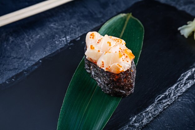 Chiuda sulla vista sui sushi gunkan con salsa piccante e scaloppina sulla superficie scura della pietra