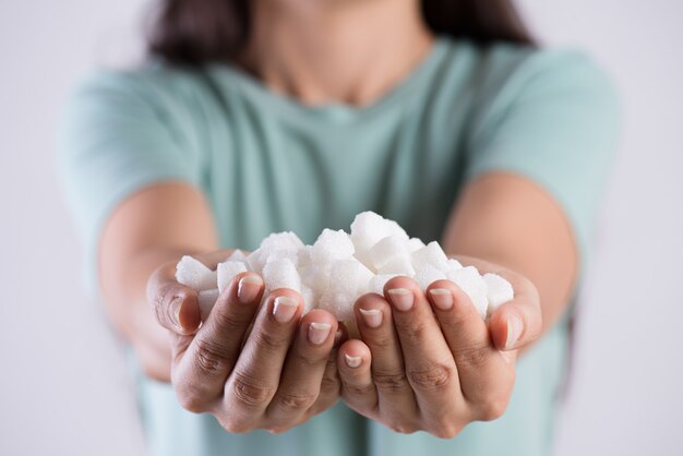 Chiuda sulle mani della donna che tengono i cubi dello zucchero bianco. Concetto di assistenza sanitaria.