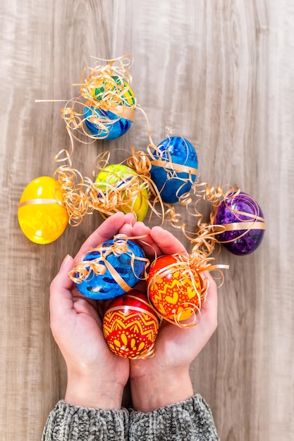 Chiuda sulle mani della donna che tiene le uova di pasqua decorate su fondo di legno