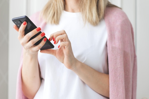 Chiuda sulle mani della donna con la manicure rossa usa uno smartphone su sfondo bianco scrivendo un messaggio di testo goditi la comunicazione online del prodotto dell'ordine di acquisto