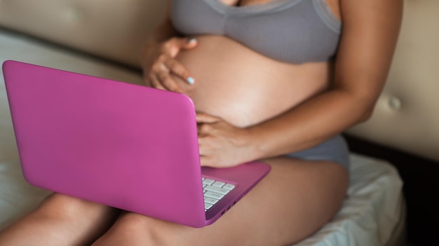 Chiuda sulle mani della donna sul computer portatile con la gravidanza avanzata della pancia grande. la ragazza incinta sfoglia il laptop