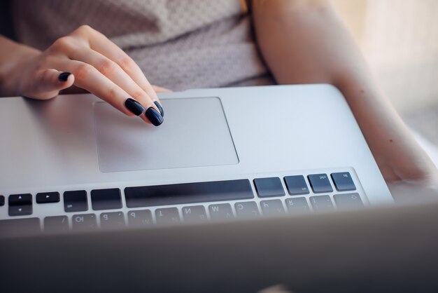 Chiuda sulle mani della giovane donna con il manicure luminoso sul touchpad del computer portatile, fuoco selettivo.