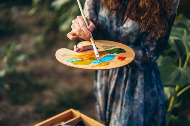 Chiuda sulle mani della spazzola e della tavolozza femminili della tenuta dell'artista con le pitture ad olio.