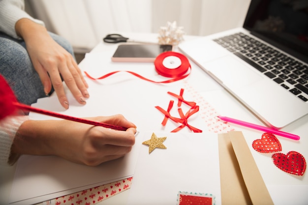 Chiuda sulle mani femminili che fanno la cartolina d'auguri per il nuovo anno e il Natale