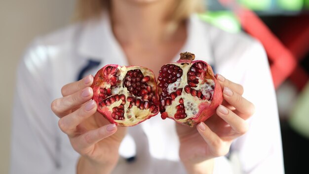 Chiuda sulle mani medico che tiene visita di frutta di melograno maturo a una vitamina di dieta di frutta nutrizionista