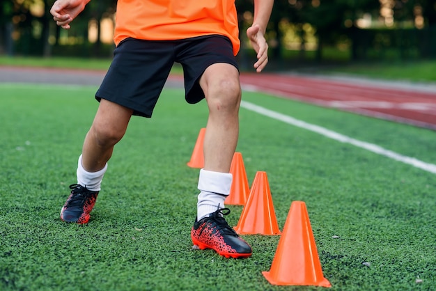 Chiudere i giocatori di calcio in esecuzione tra i coni di plastica arancione