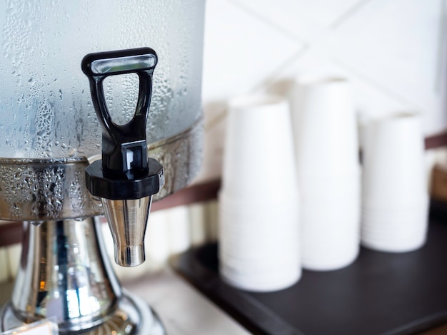 Chiudere il rubinetto più fresco per l'acqua potabile fredda vicino a pile di servizio di tazza di carta bianca vuota gratuitamente per il cliente nella caffetteria.