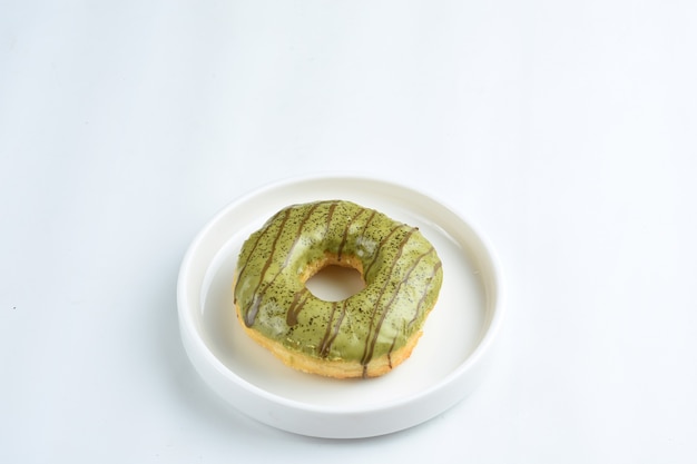 Chiudere la ciambella con guarnizione di tè verde in piatto bianco isolato su bianco