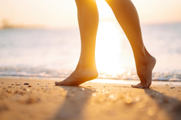 Chiudere la gamba della giovane donna che cammina lungo l'onda di acqua di mare e sabbia sulla spiaggia estiva