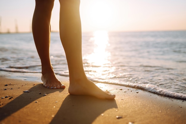Chiudere la gamba della giovane donna che cammina lungo l'onda di acqua di mare e sabbia sulla spiaggia estiva