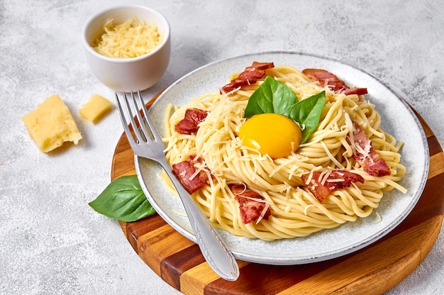 Chiudere la tradizionale pasta italiana alla carbonara con pancetta, formaggio e tuorlo d'uovo su piastra su sfondo chiaro.