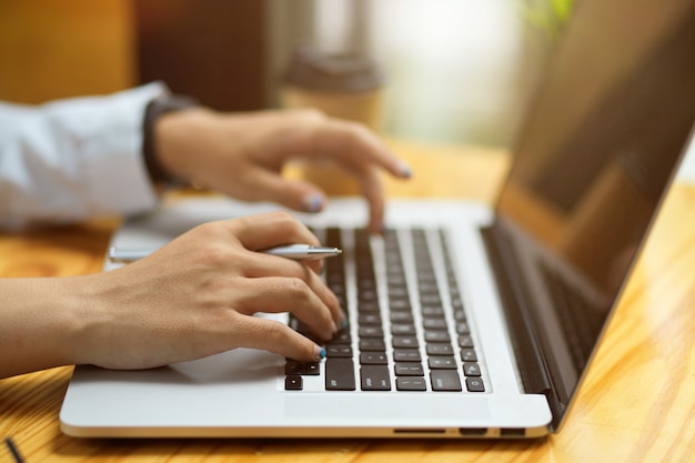 Chiudere le mani femminili digitando, navigando, facendo assegnazione sulla tastiera del laptop su un tavolo di legno