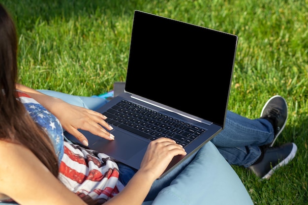 Chiudere le mani sulla tastiera. Donna che lavora al computer pc portatile con schermo vuoto nero vuoto per copiare lo spazio nel parco sul prato del sole dell'erba verde all'aperto.