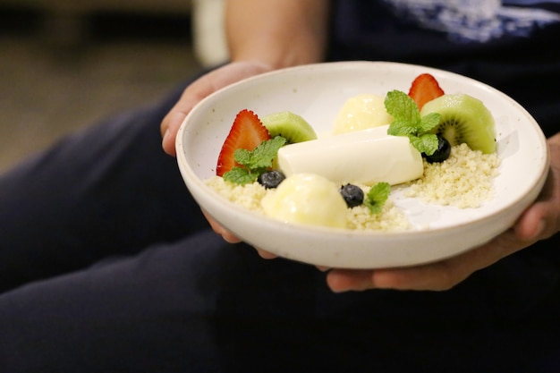 Chiudere le mani tenendo la cotta di pana con gelato alla fragola, kiwi e ananas