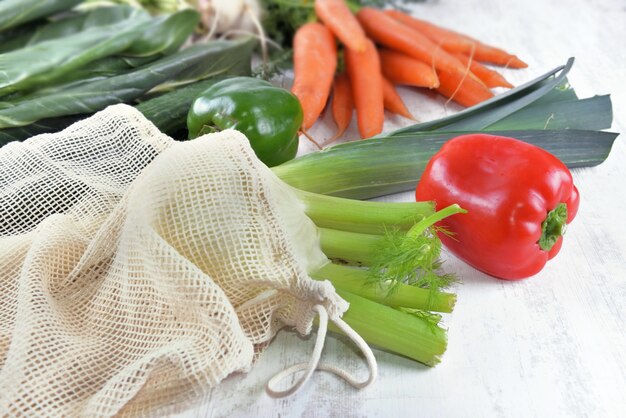 Chiudere le verdure in un sacchetto riutilizzabile e altre verdure fresche su un tavolo bianco