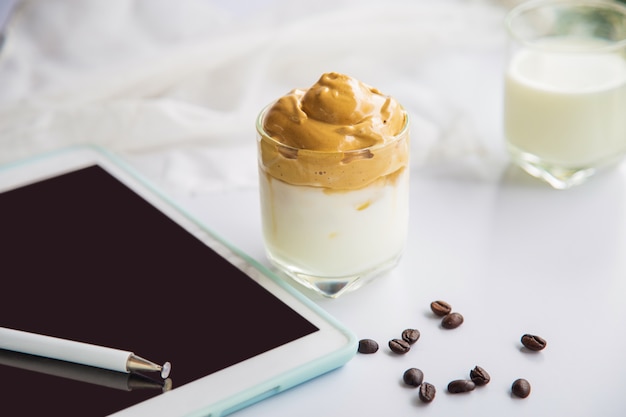 Chiudere una tazza di caffè Dalgona con chicchi di caffè accanto a una tavoletta su un tavolo bianco