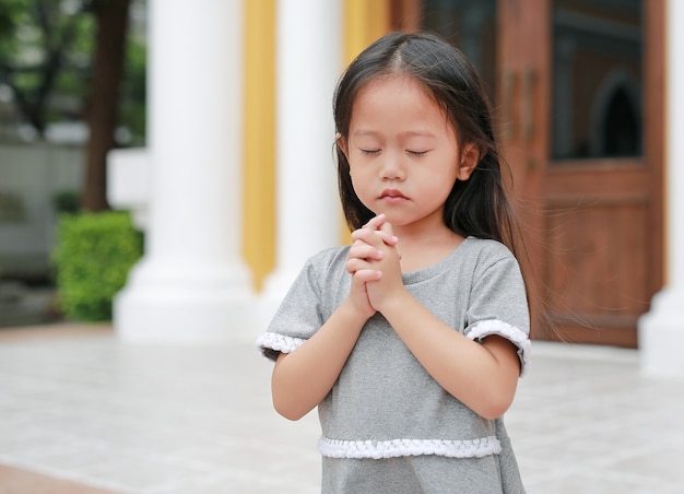 Chiudi gli occhi piccola ragazza asiatica che prega in chiesa